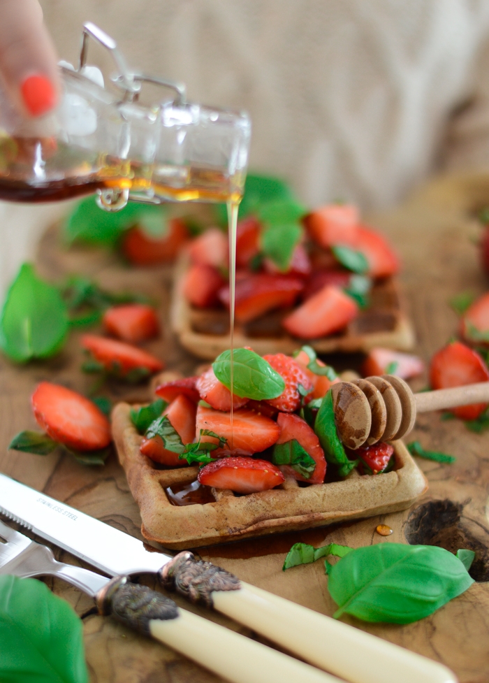 Pouring maple syrup over waffles and strawberries