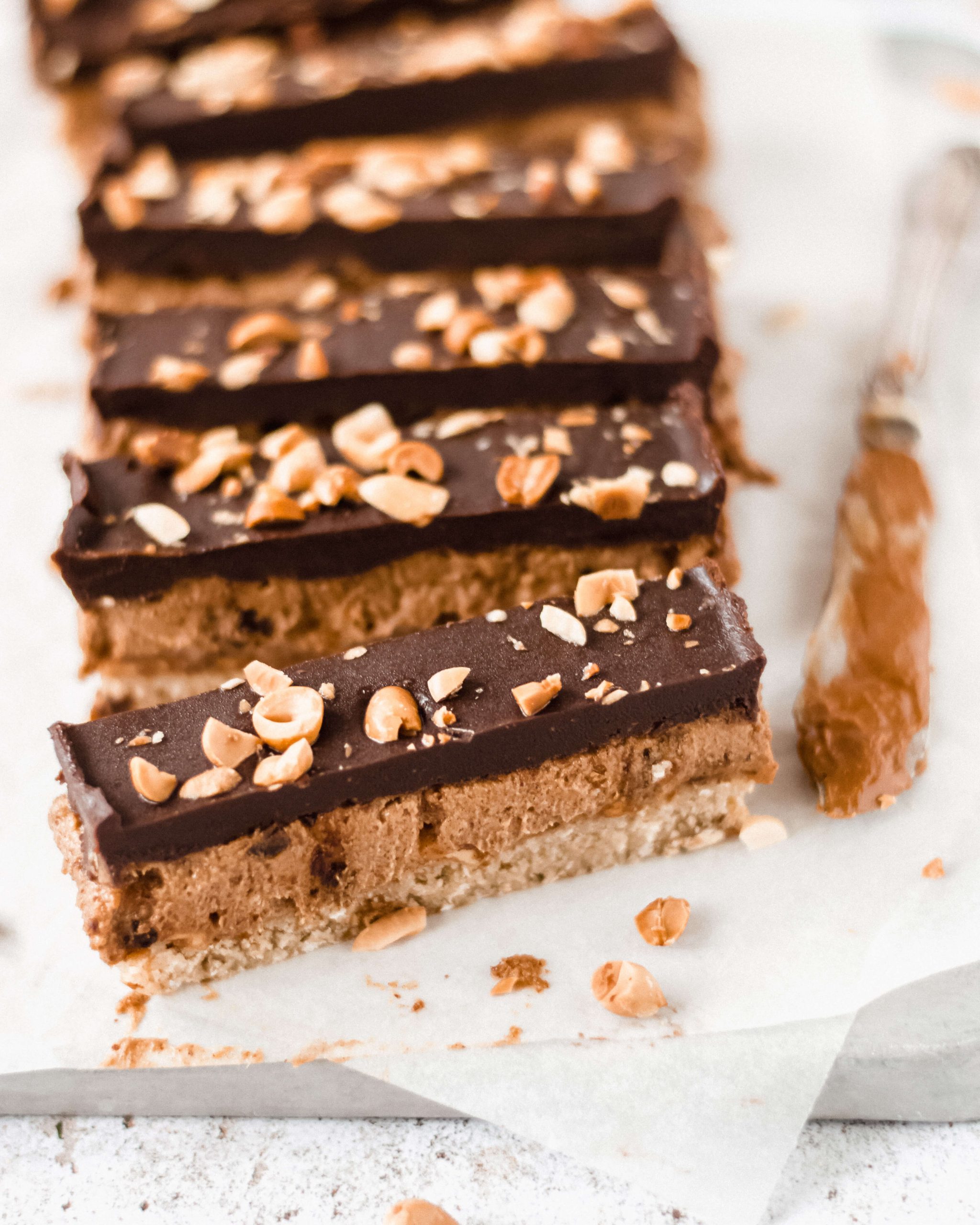 Close up view of vegan peanut and caramel bars with nuts, knife on the side 