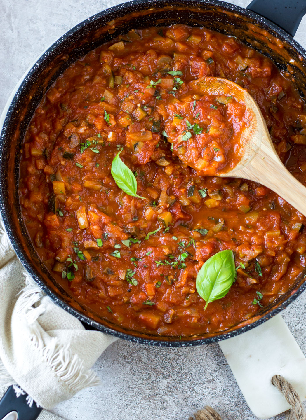 Top down view marinara sauce in a black saucepan with wooden spoon