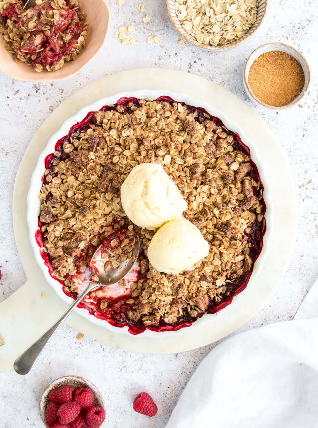 Raspberry & Rhubarb Crisp with ice cream in a white pie dish 