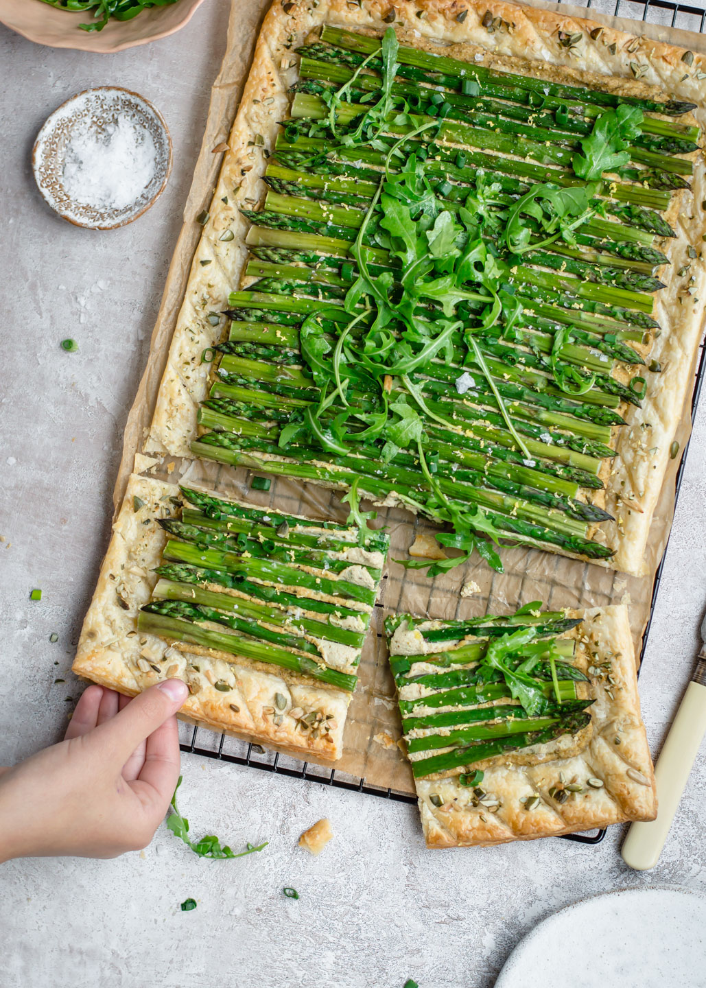 Top down view of asparagus tart with a hand reaching for the slice