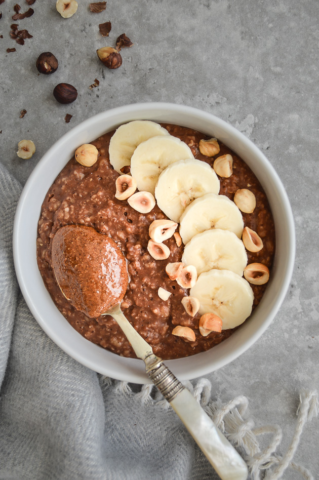 Nutella porridge bowl topped with sliced bananas, hazelnuts & a spoonful of nut butter