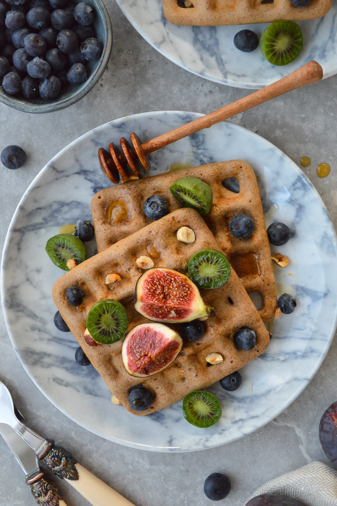 Pumpkin spice waffles on a plate topped with figs, kiwi, blueberries & nuts 
