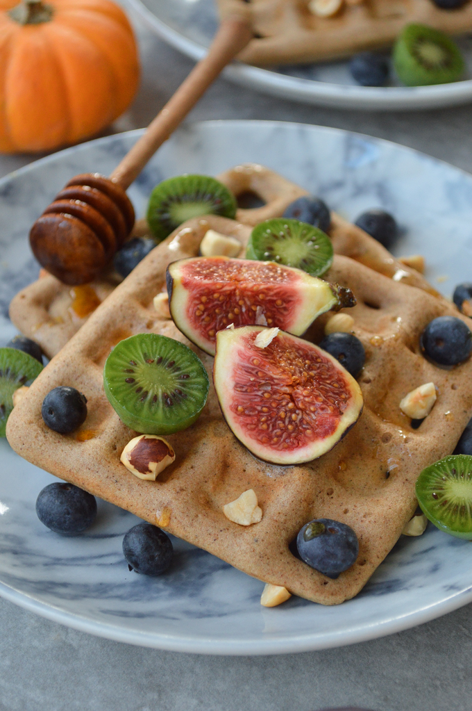 Pumpkin spice waffles on a plate topped with figs, kiwi, blueberries & nuts 