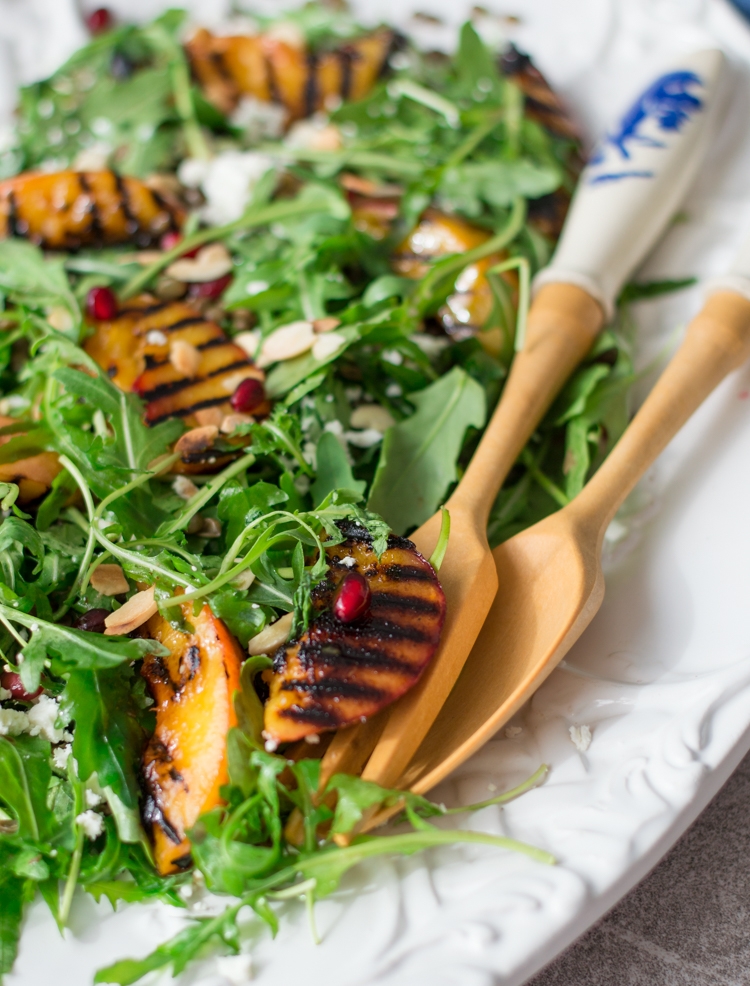 A white plate with grilled nectarines, arugula, lentils & salad serving spoons 