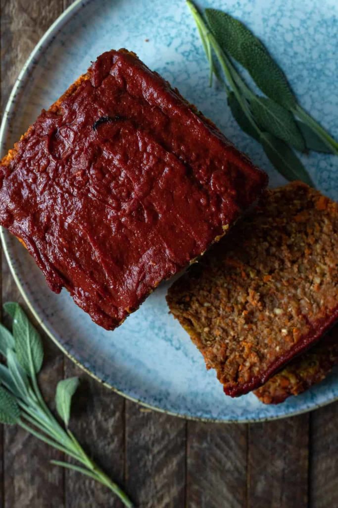 Top down view of vegan lentil and carrot loaf glazed with red sauce on a plate, sage leaves around it