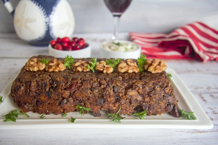 Close up of Keto Mushroom Walnut Loaf on a white table, cranberries and wine glass behind