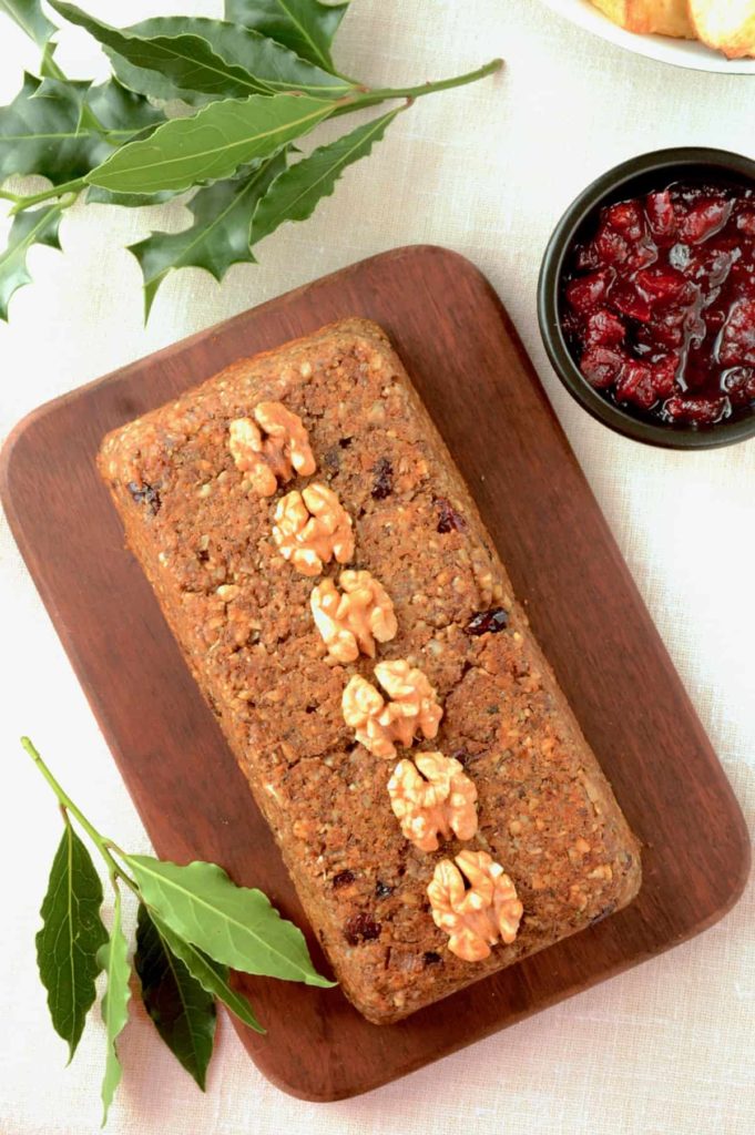 Top down view of vegan nut roast loaf decorated with walnuts on a wooden board, cranberry sauce on side