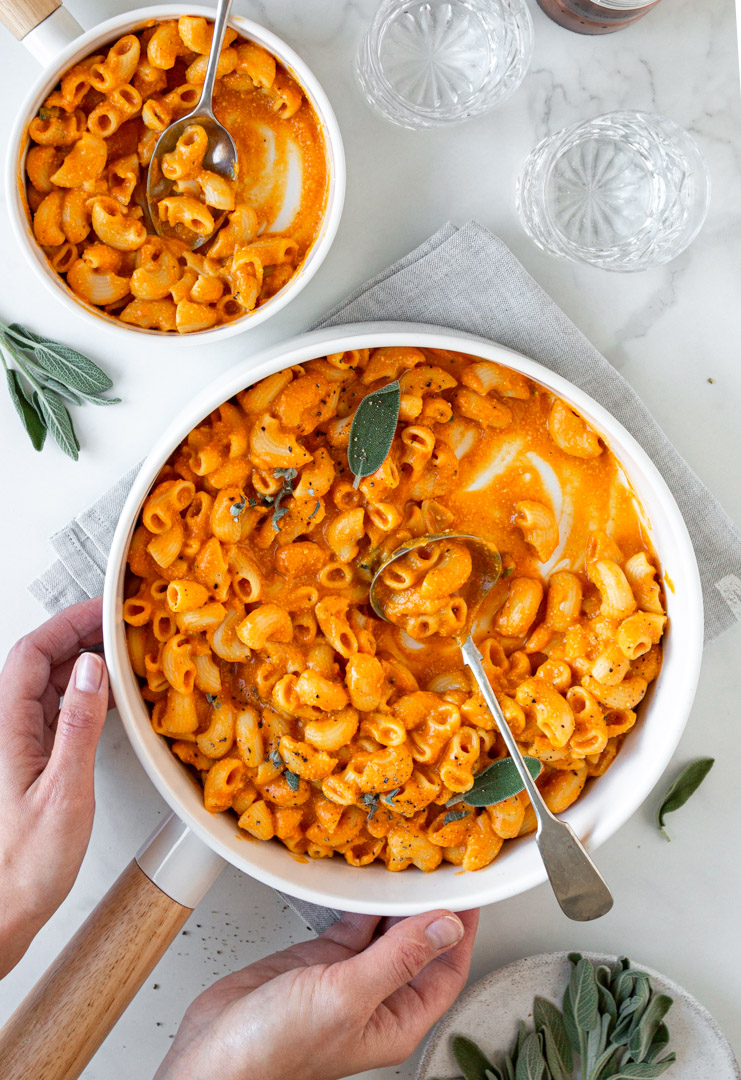 Overhead view of vegan mac and cheese in a white bowl , hands holding the bowl 