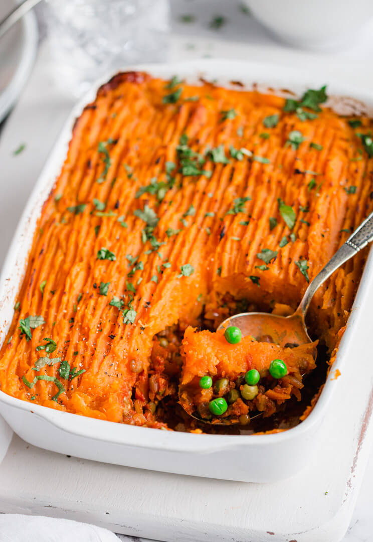 Close view of vegan shepherd's pie in a white dish, spoon on the side 
