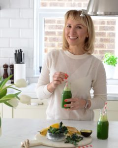 Tania in the white kitchen, holding a green smoothie 