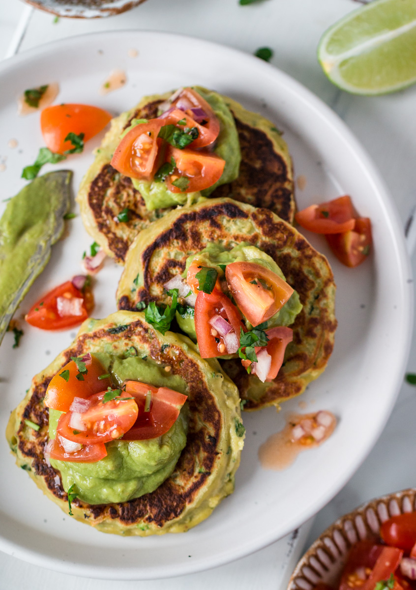 Top down view of savoury vegan pancakes topped with guacamole and tomato salsa 
