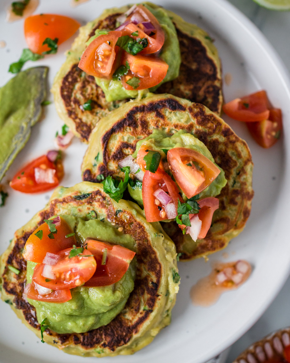 Top down view of savoury vegan pancakes topped with guacamole and tomato salsa 