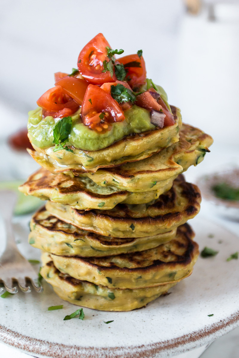A stack of savoury vegan pancakes topped with guacamole and tomato salsa 