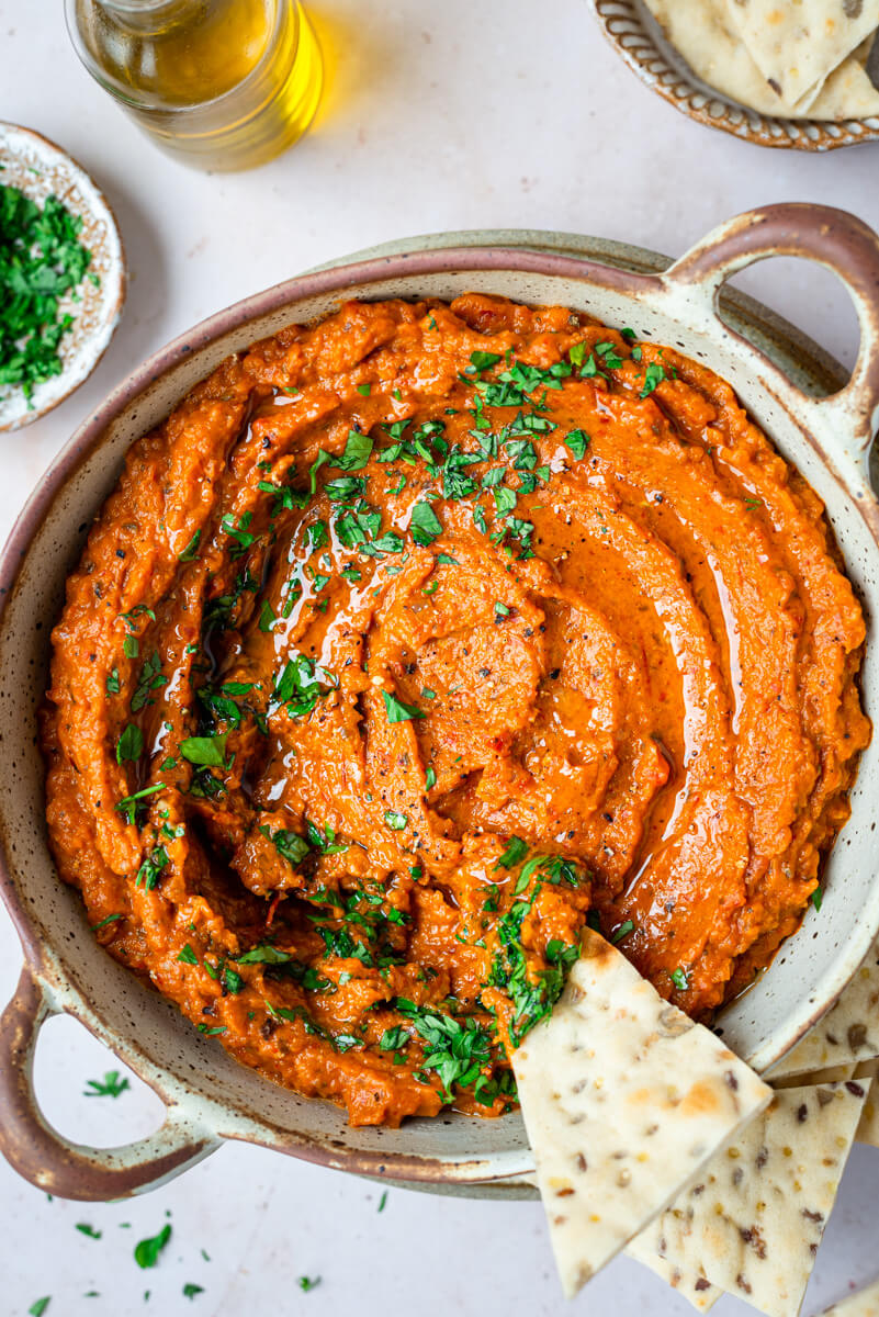 Top down view of aubergine & red pepper dip in a brown bowl with pita bread 