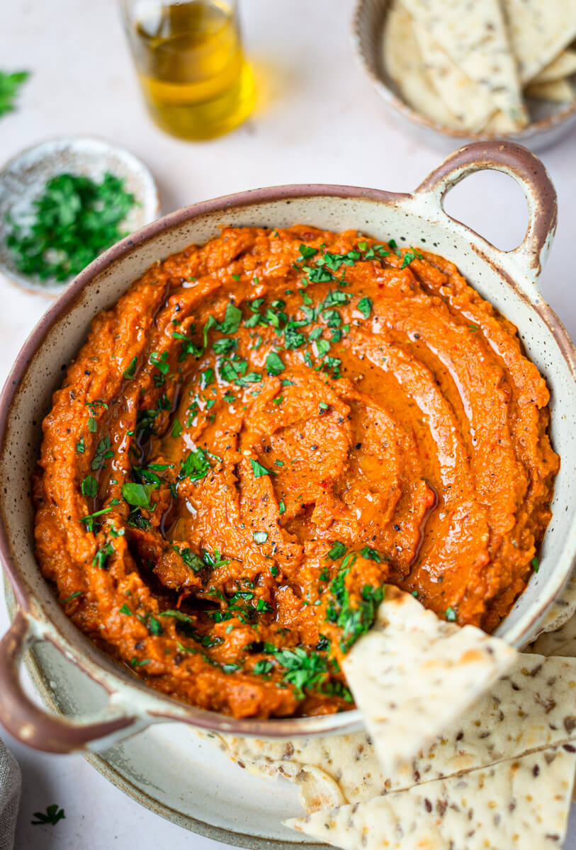 Top down view of aubergine & red pepper dip in a brown bowl with pita bread 