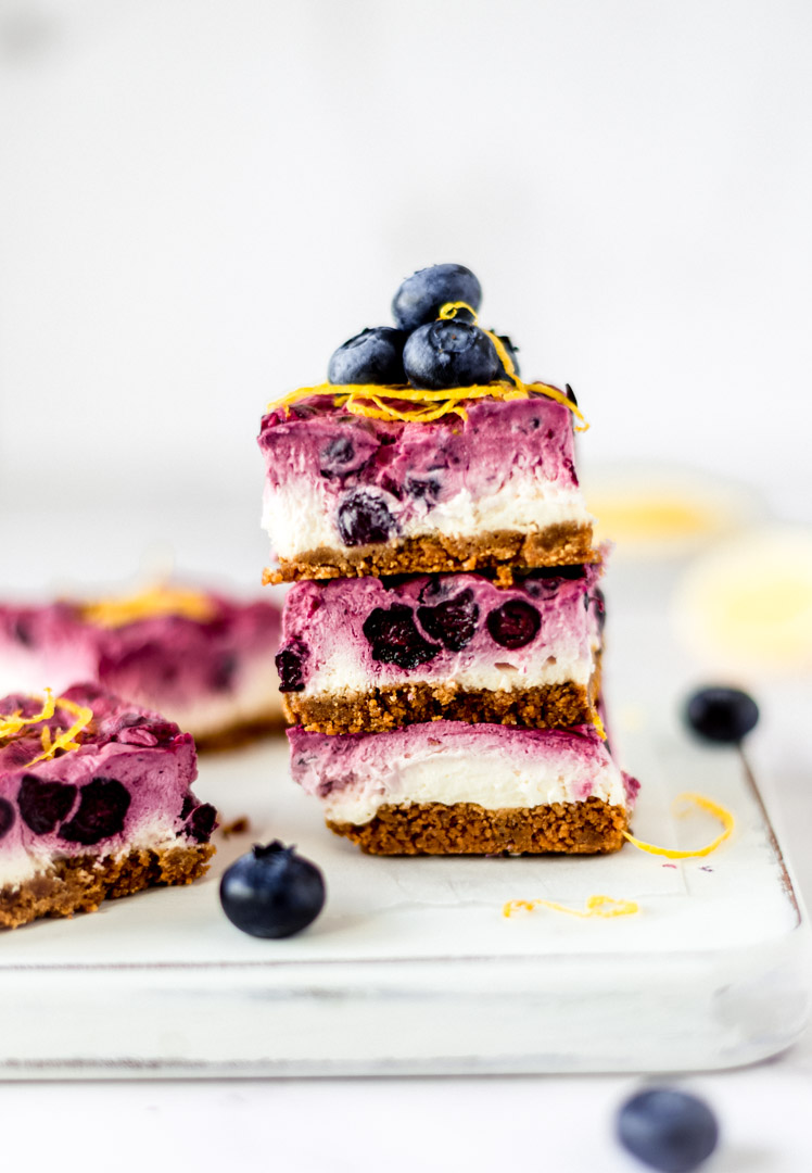 A stack of vegan blueberry lemon cheesecake bars on a white board