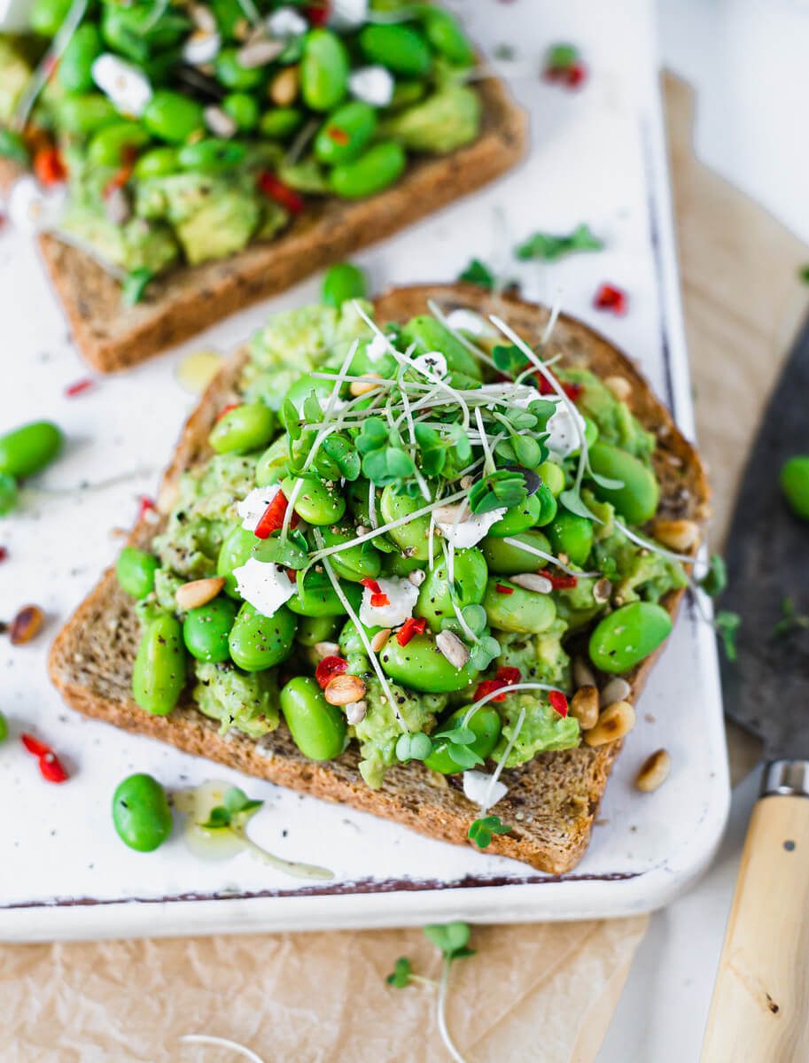 Vegan avocado toast with edamame beans & feta on a white board  