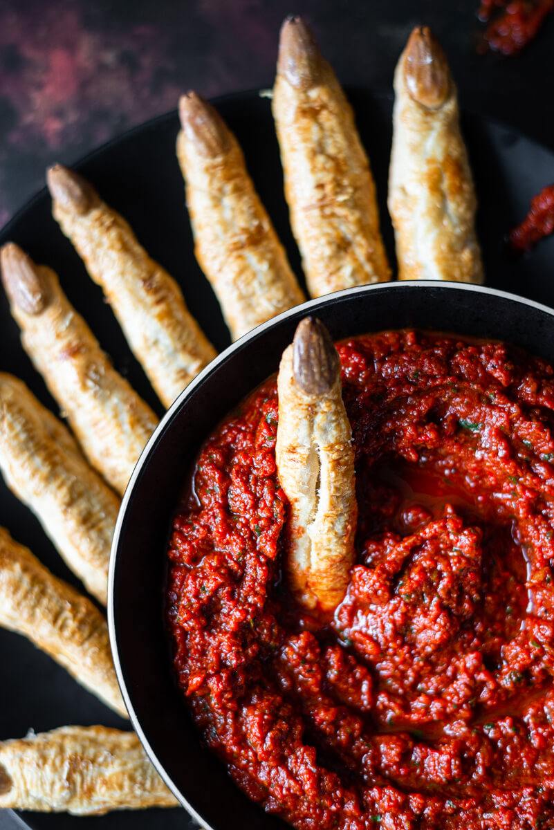 Witches’ finger breadsticks on a black plate with red pepper dip 