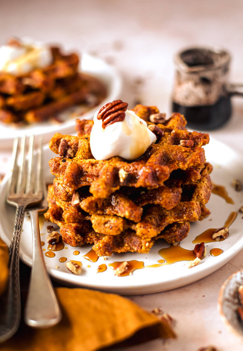 Pumpkin waffles on a white plate topped with pecans, yoghurt and maple syrup  