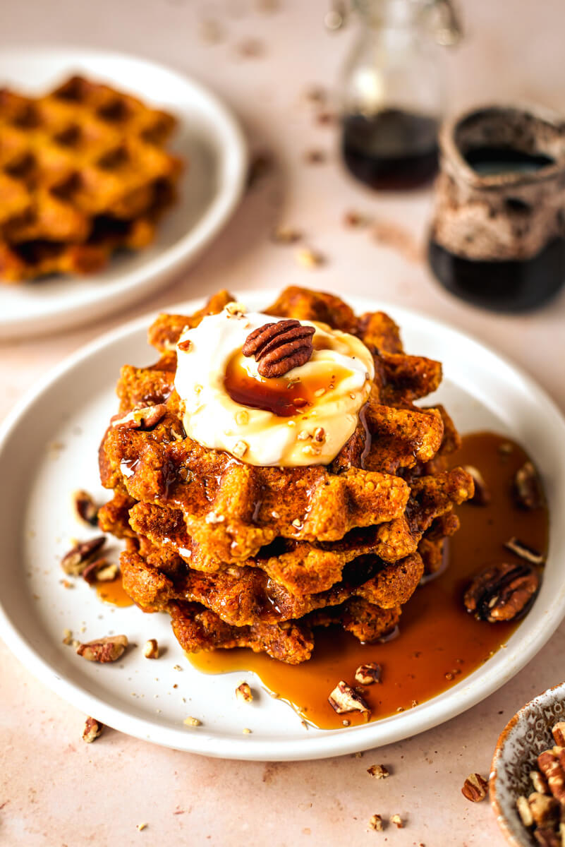 Pumpkin waffles on a white plate topped with pecans, yoghurt and maple syrup  