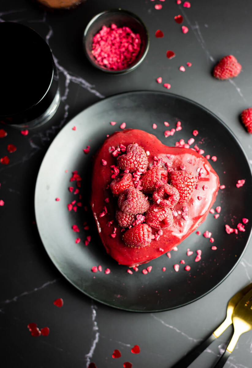 Heart-shaped vegan Valentine’s cheesecake with raspberries on a black plate 