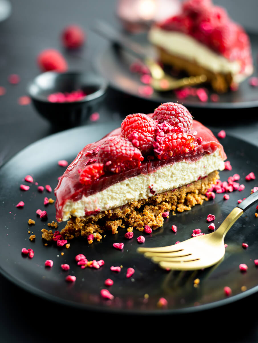 A slice of heart-shaped vegan Valentine’s cheesecake with raspberries on a black plate 
