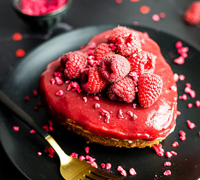 Heart-shaped vegan Valentine’s cheesecake with raspberries on a black plate